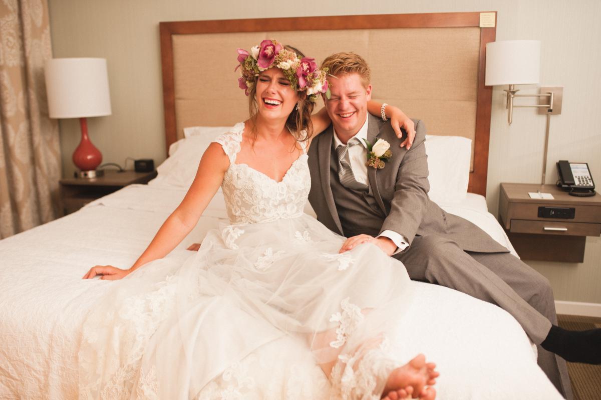 Bride and Groom Laughing Seated on Hotel Room Bed